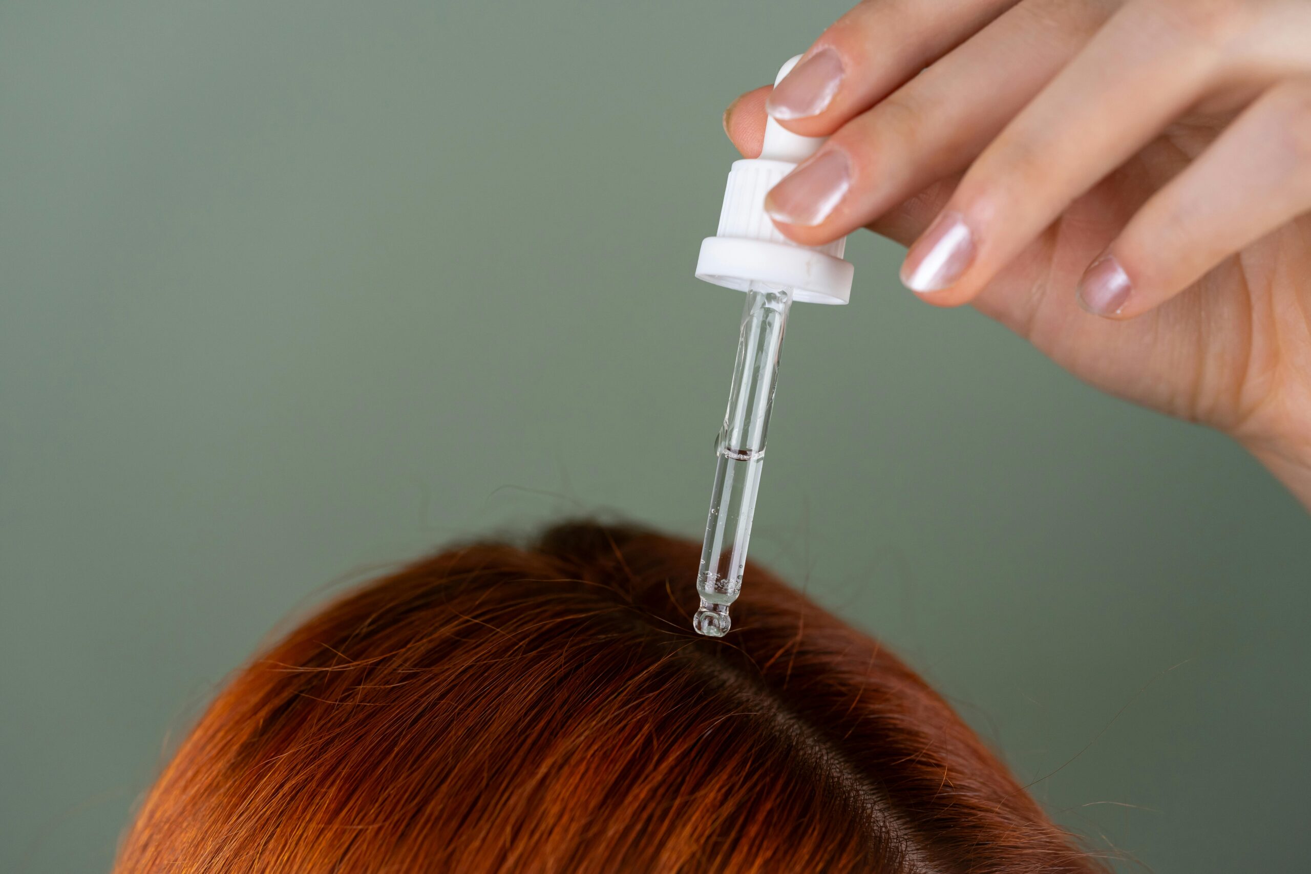 A woman applies hair serum to style her hair, holding the canister with one hand and her hair with the other.
