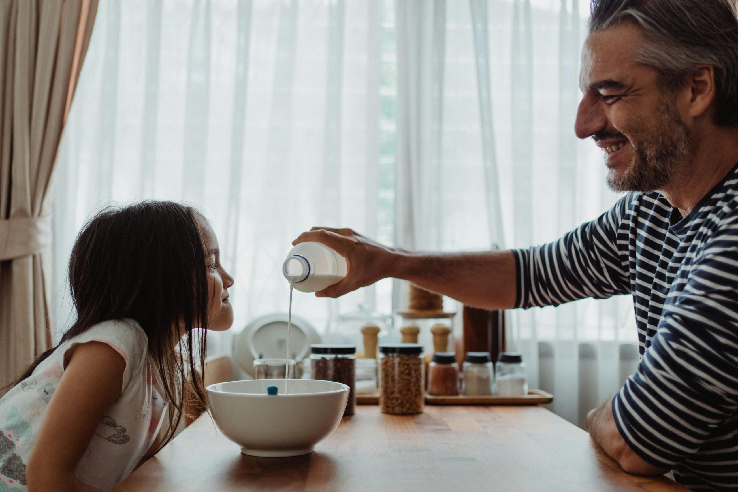 A man and a young girl sit at a table, enjoying breakfast together with a bowl of cereal in front of them.