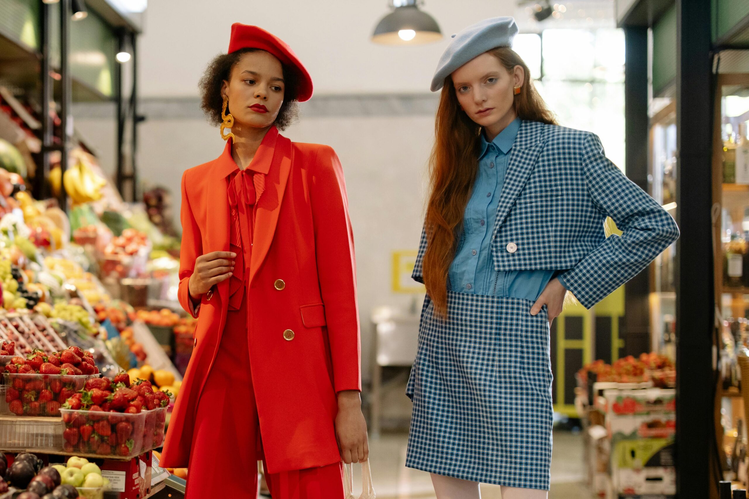 Two women in red and blue outfits stand together in a supermarket aisle, surrounded by shelves of groceries.