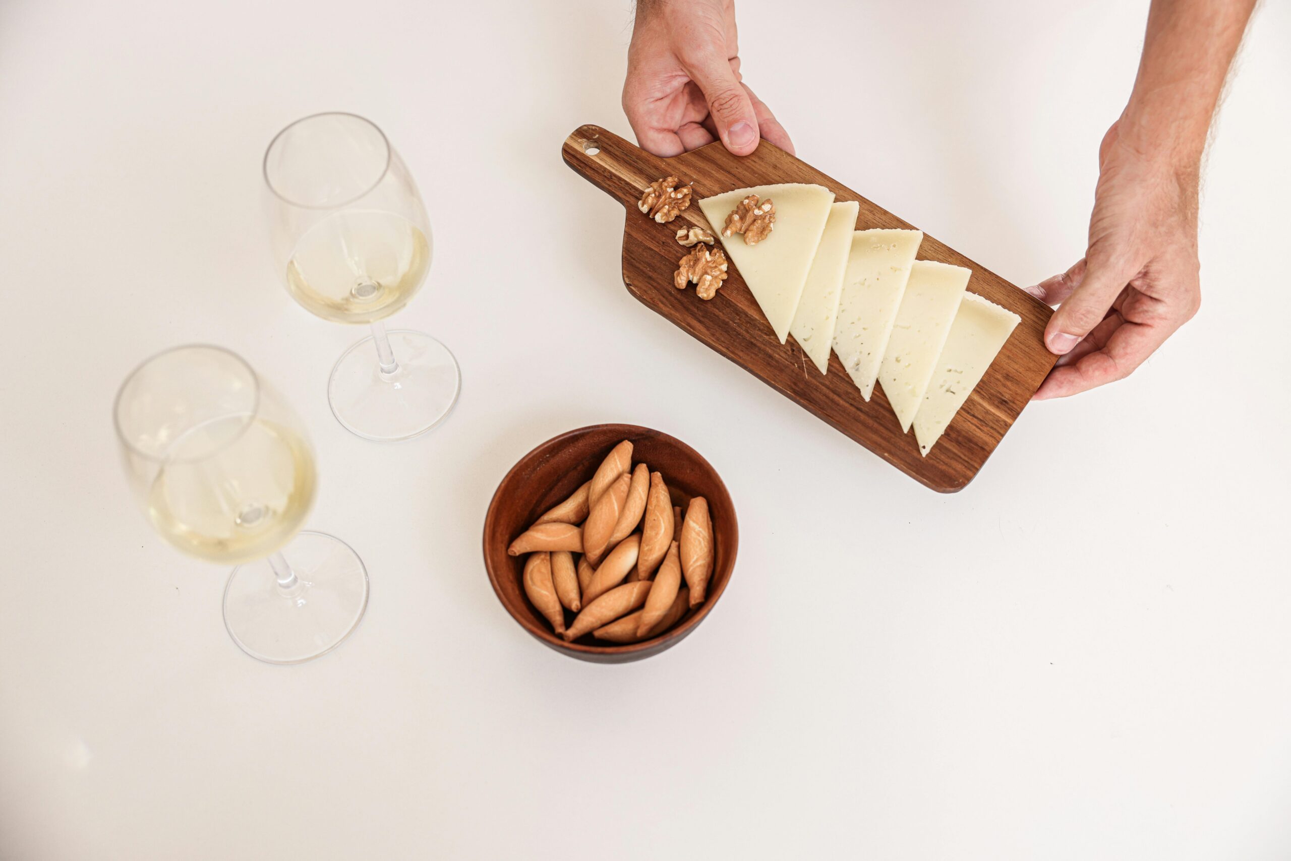 A person presenting a cheese board adorned with various cheeses, nuts, and a glass of wine.