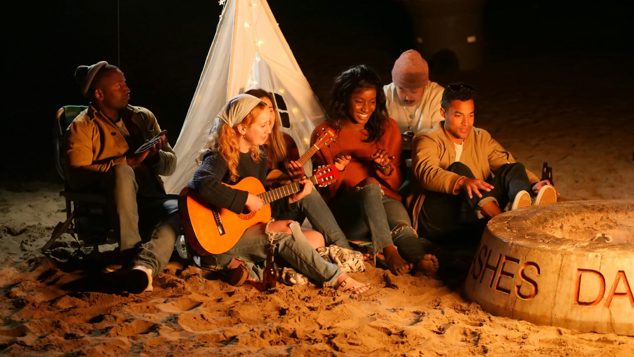 A group of people gathered around a campfire, playing guitars and enjoying each other's company under the night sky.