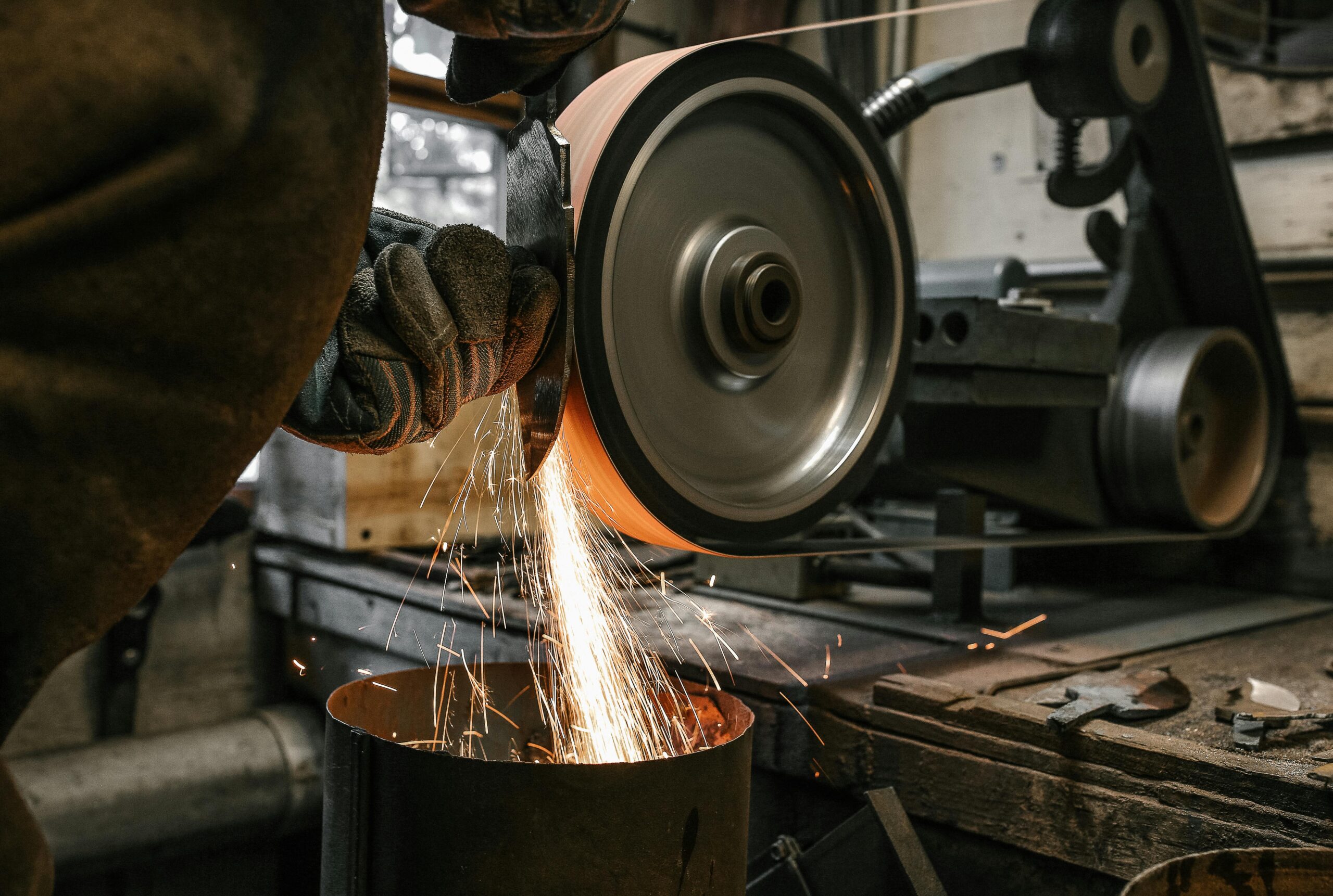A person using a grinder to grind metal, sparks flying as they work in a workshop setting.