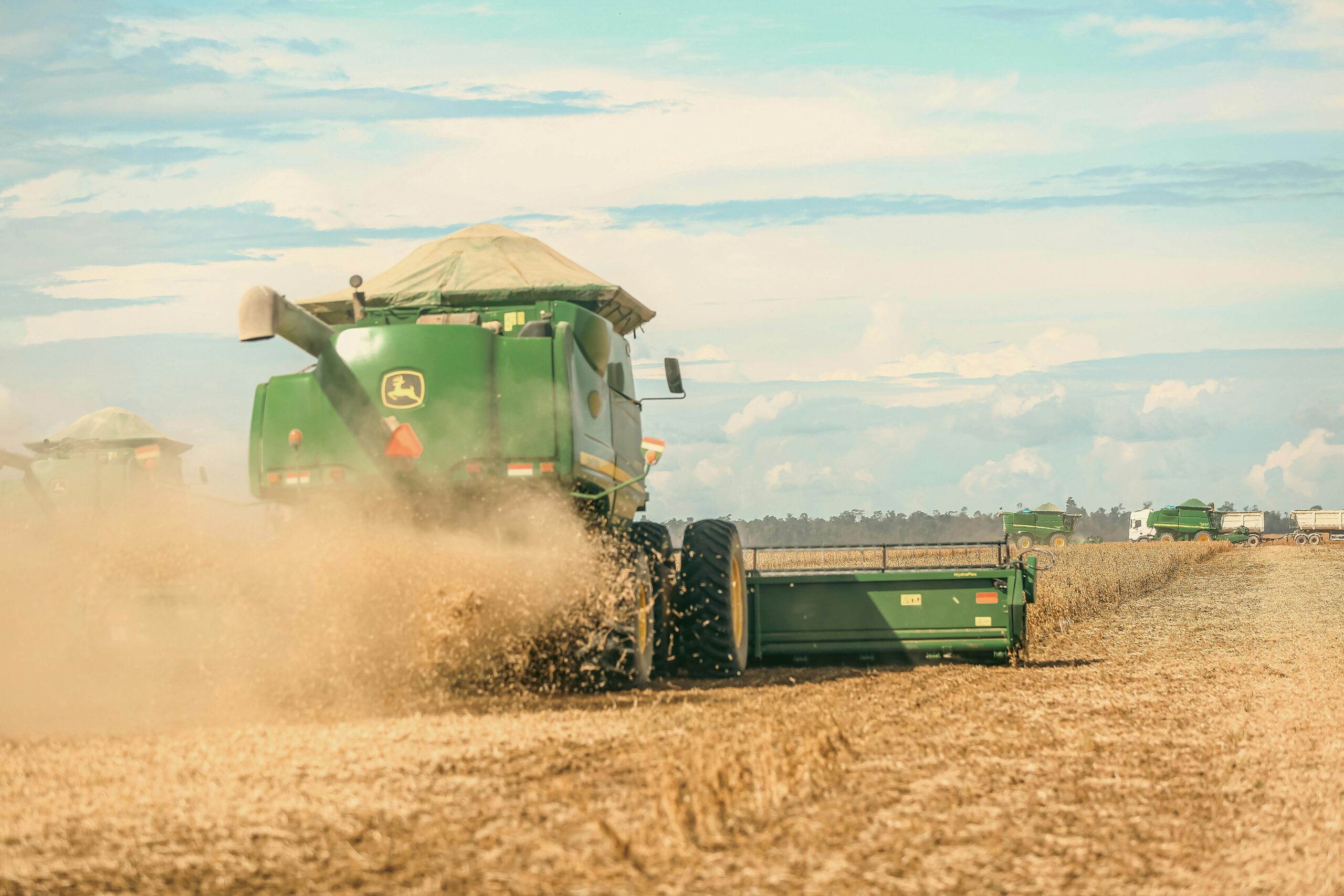 A combine harvester operates in a vast field, harvesting crops under a clear blue sky.