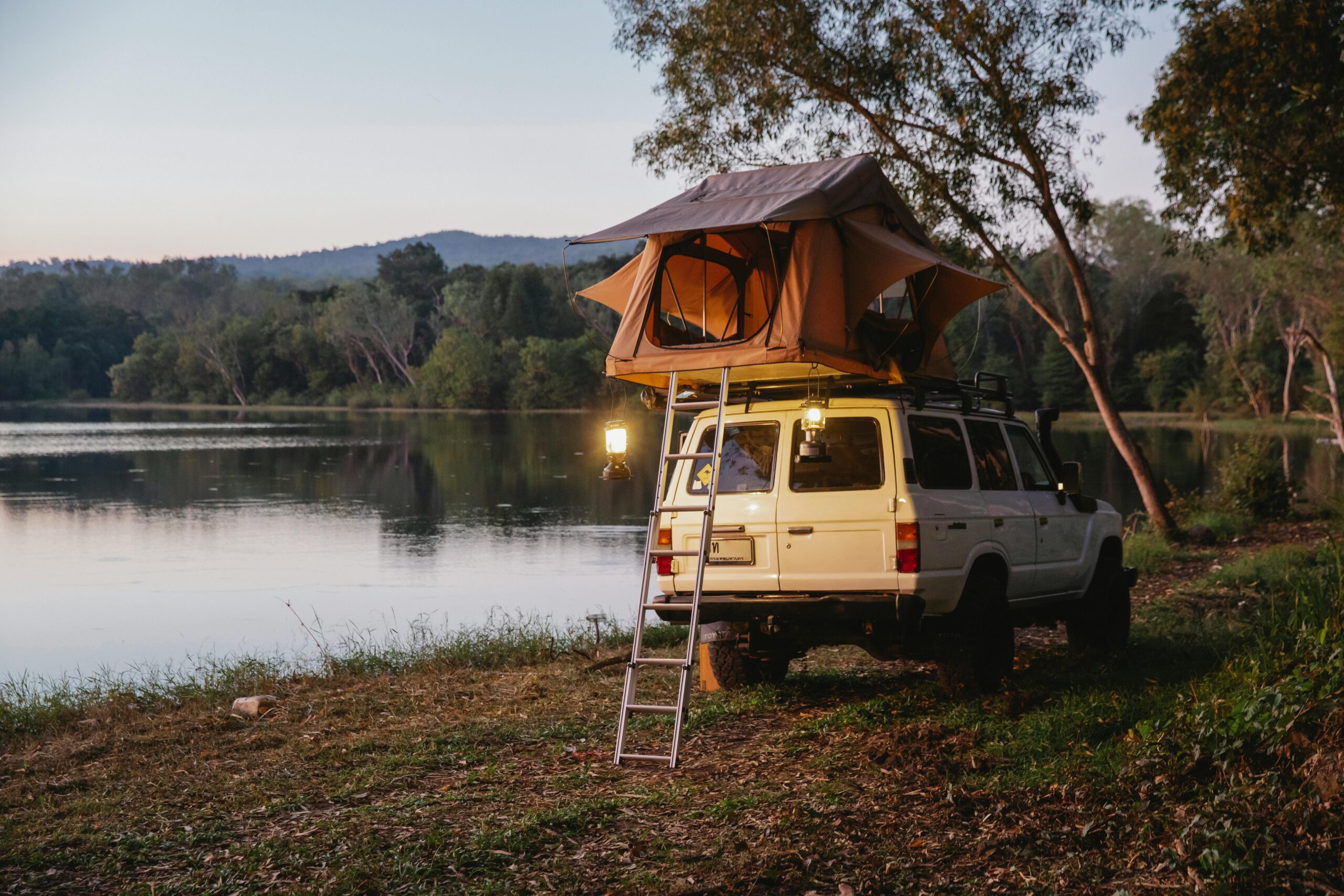 A vehicle with a rooftop tent parked beside a serene lake, surrounded by trees and reflecting water.