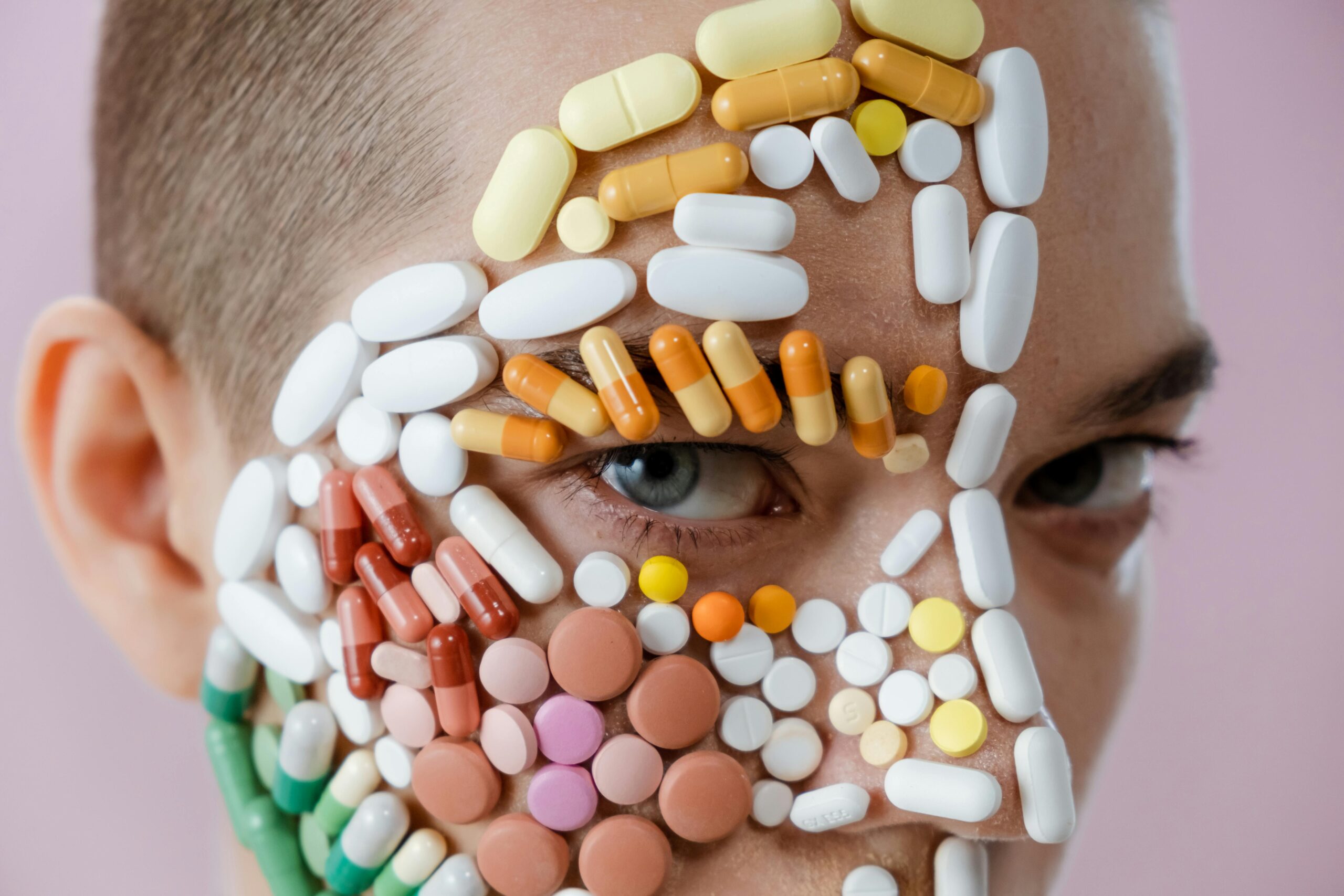 A man with various pills arranged on his face, creating a surreal and artistic visual effect.