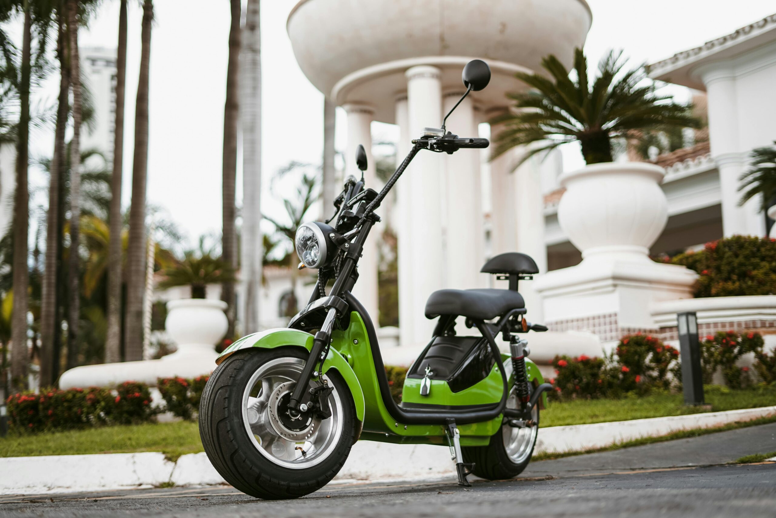 A green electric scooter parked in front of a modern building with large windows.